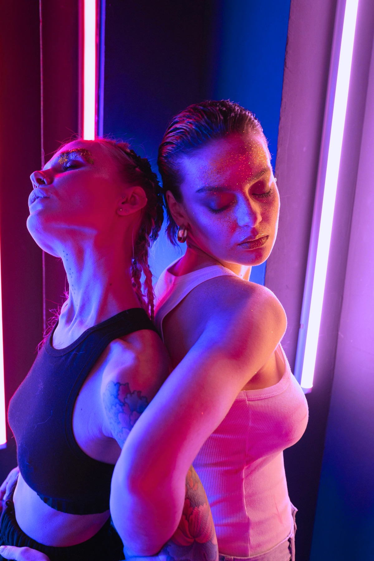 Queer couple posed back to back under neon lights